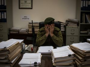 לוחם במדים יושב מתוסכל מול שולחן עם ערימת מסמכים משפטיים, מסמל את המאבק בביורוקרטיה של משרד הביטחון.